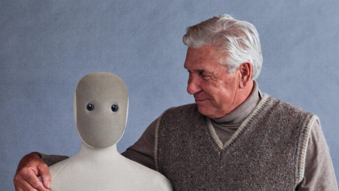 1X NEO humanoid robot in a beige knit suit beside a smiling older man in a sweater vest who has his arm around the robot