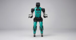 Agility Robotics Digit 5 humanoid robot standing front-facing in a gray studio, teal torso and black head with chest display