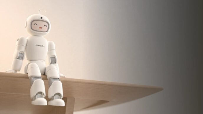 AiMOGA's Mobo, a small white humanoid home robot with a rounded helmet-like head and a smiling face on its display, sitting on the edge of a wooden table against a warm beige wall