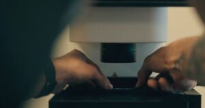 Close-up of two hands loading a sample into a laboratory microscope