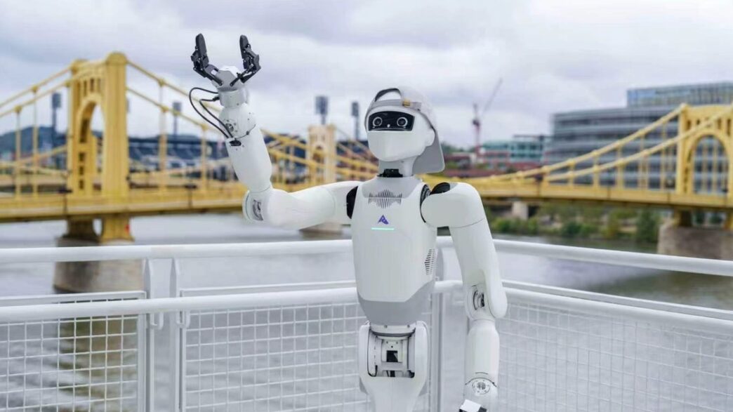 White Astribot T1 robot with a black visor-style face and a cap, one gripper raised, at a riverside railing in front of a yellow suspension bridge
