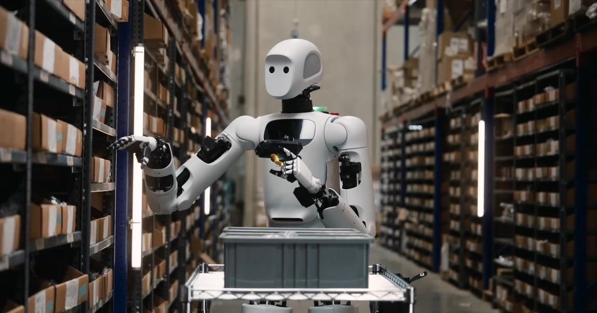 Apptronik Apollo humanoid robot in a warehouse aisle reaching toward shelving while holding a barcode scanner, head visible