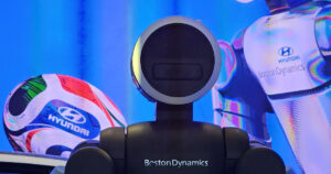 Close-up of the torso and round, ring-lit head of a Boston Dynamics Atlas humanoid robot with the Boston Dynamics name on its chest