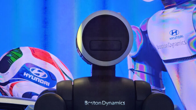 Close-up of the torso and round, ring-lit head of a Boston Dynamics Atlas humanoid robot with the Boston Dynamics name on its chest