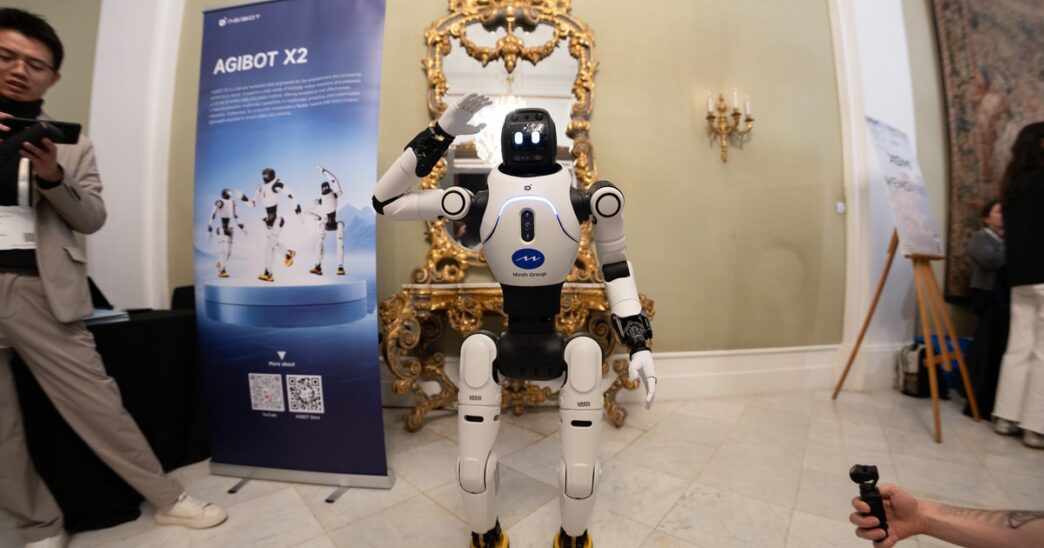 White AgiBot X2 humanoid robot waving at an exhibition stand in an ornate hall at MWC 2026 in Barcelona, with visitors filming it