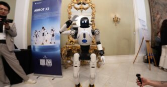 White AgiBot X2 humanoid robot waving at an exhibition stand in an ornate hall at MWC 2026 in Barcelona, with visitors filming it