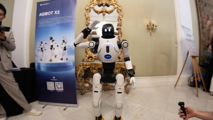White AgiBot X2 humanoid robot waving at an exhibition stand in an ornate hall at MWC 2026 in Barcelona, with visitors filming it