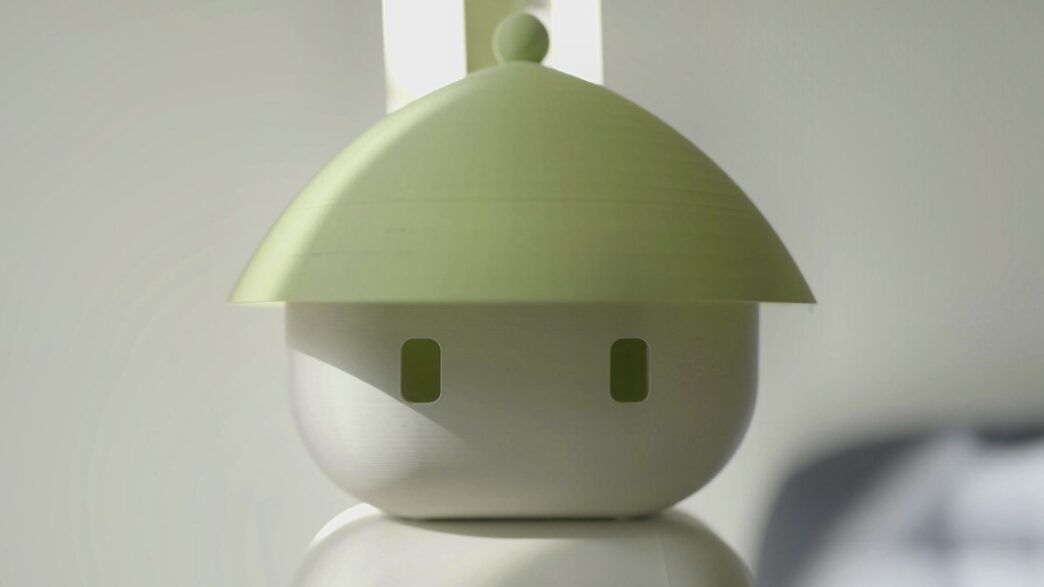 Close-up of the Flourish 1 home robot's round white head with two small rectangular eyes under a wide pale-green conical hat