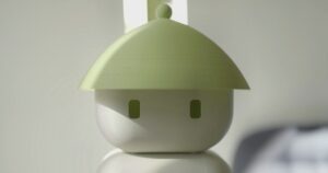 Close-up of the Flourish 1 home robot's round white head with two small rectangular eyes under a wide pale-green conical hat