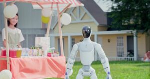 White Galbot ET1 humanoid robot with a glossy black visor standing on a lawn beside a pink-striped drinks stand with balloons, a smiling girl behind the stall