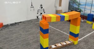 White Galbot humanoid robot stands behind an arch of oversized orange, yellow and blue blocks in a lab with a GALBOT watermark