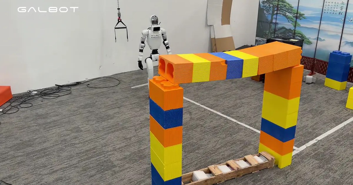 White Galbot humanoid robot stands behind an arch of oversized orange, yellow and blue blocks in a lab with a GALBOT watermark