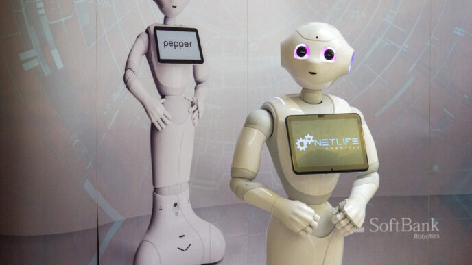White Pepper humanoid robot by SoftBank Robotics with a tablet screen on its chest, standing in front of a second Pepper