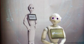 White Pepper humanoid robot by SoftBank Robotics with a tablet screen on its chest, standing in front of a second Pepper
