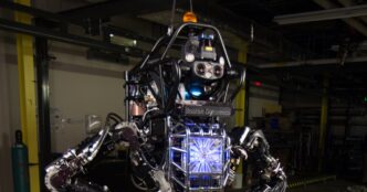 Hydraulic Boston Dynamics Atlas humanoid from the DARPA program in a test bay, exposed hydraulic joints, hoses and sensor head visible
