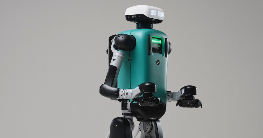 Agility Robotics Digit humanoid with a teal torso and white head unit, arms bent forward, against a grey studio backdrop