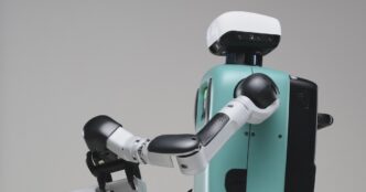 Close view of an Agility Robotics Digit humanoid reaching forward with one jointed arm, teal torso and white head unit against a grey backdrop