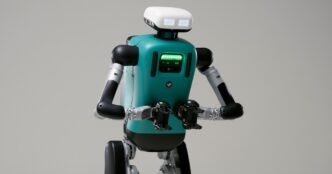 Agility Robotics Digit humanoid with a teal torso, glowing green chest lights and white head unit, against a grey studio backdrop