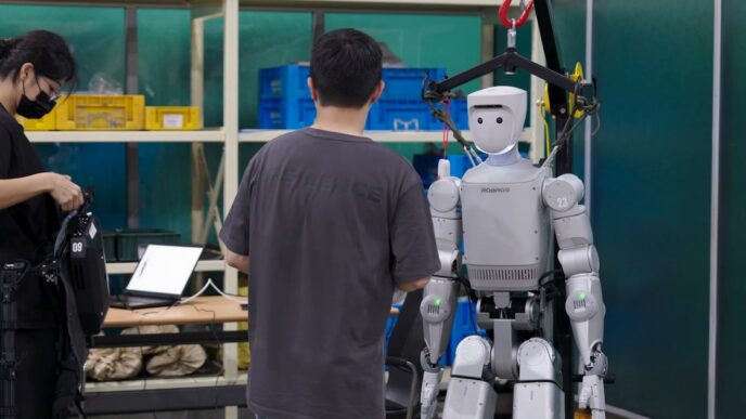 Robros IGRIS-C humanoid robot hanging from an overhead safety gantry while engineers work beside it, one wearing a teleoperation rig