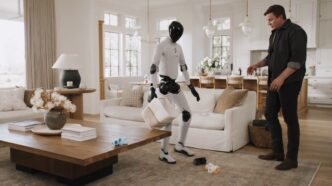 White Figure 03 humanoid robot carrying a fabric basket while tidying toys in a bright living room as a man in a dark shirt watches beside a sofa