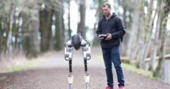 Cassie bipedal robot on a forest path beside a researcher holding a remote control