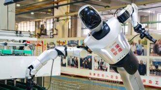 Humanoid robot placing an auto part at a workstation on a Hangzhou auto-parts production line, photographed October 13, 2026