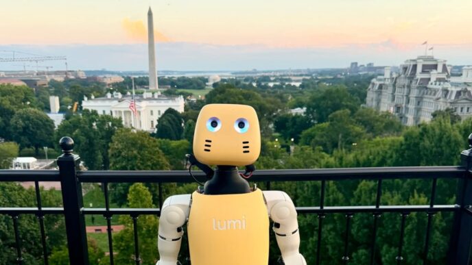 A small cream and yellow Lightberry Lumi humanoid robot with round blue eyes standing at a black railing on a rooftop in Washington, DC, with the Washington Monument and the White House grounds behind it at sunset