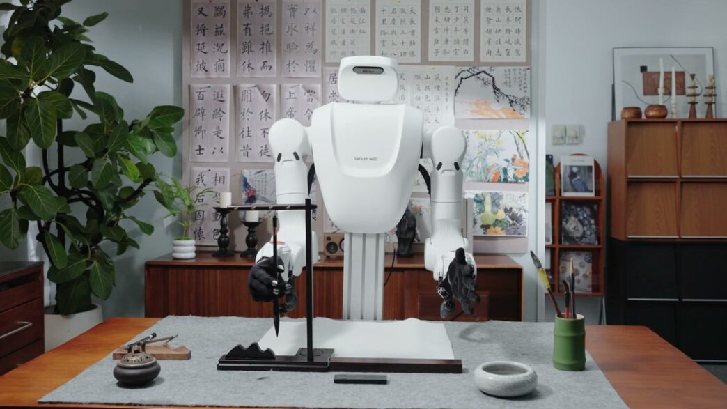 Nature Will dual-arm robot with dexterous hands holding a calligraphy brush at a desk in the Natura-1 demo