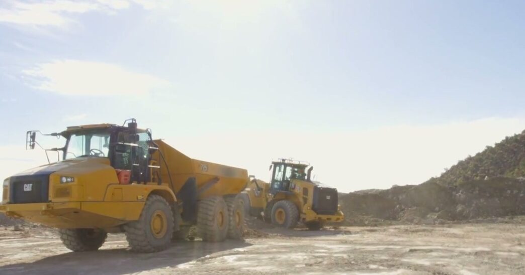 Yellow CAT wheel loader and articulated dump truck on a dusty Utah worksite, from Physical Intelligence's Actor partner demo for the Pi API beta
