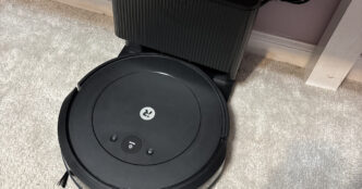Black iRobot Roomba Combo 2 Essential robot vacuum docked at its charging station on a light carpet