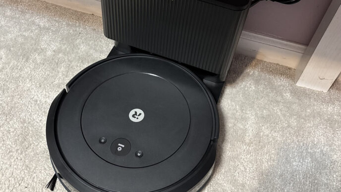 Black iRobot Roomba Combo 2 Essential robot vacuum docked at its charging station on a light carpet