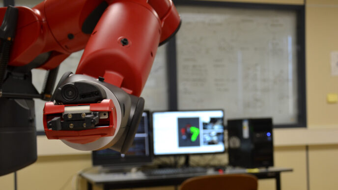 Close-up of a Rethink Robotics Baxter robot arm and its parallel-jaw gripper holding a small circuit board in a lab