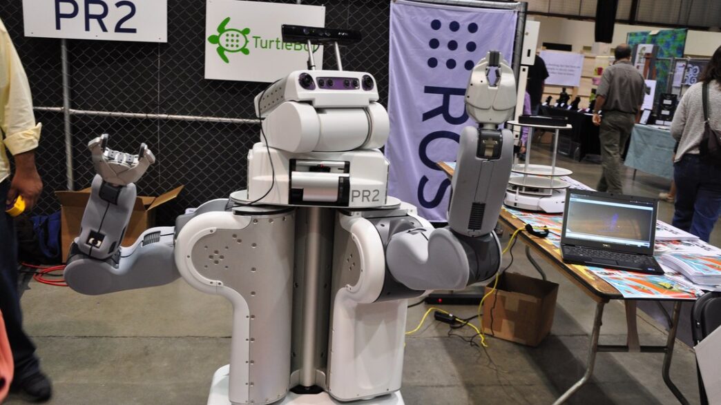 Willow Garage PR2 research robot, a white two-armed mobile robot with a camera-equipped head, shown at an exhibition