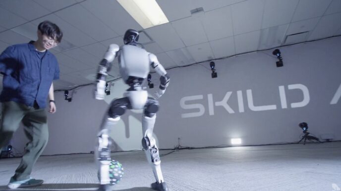 A white bipedal humanoid robot controls a soccer ball while a man defends, in front of a Skild AI wall logo