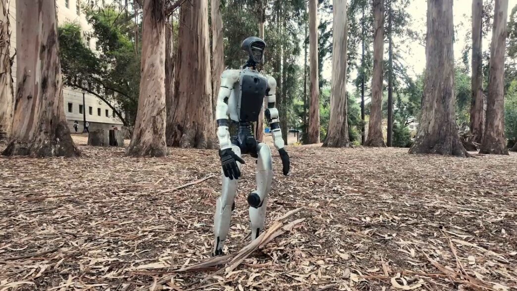 White Unitree G1 humanoid robot standing on a carpet of dry eucalyptus leaves among tall eucalyptus trees, from the SuperMimic project video