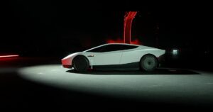 Side profile of the white second-generation Tesla Roadster under a spotlight on a dark stage, with a red-lit ramp behind it