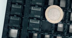 Four black Ubitium UB108 processor chips in a JEDEC tray beside a one-euro coin for scale