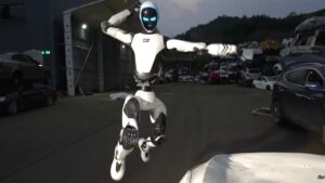 Unitree's white H2-X humanoid robot with a dark visor and glowing blue eyes leaping in mid-air with fists raised in a scrapyard at dusk