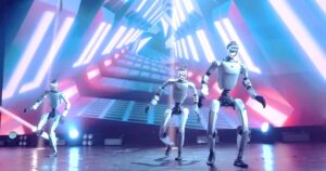 Three Unitree humanoid robots dancing on a stage with LED lighting in Unitree's UniUni swarm control launch video