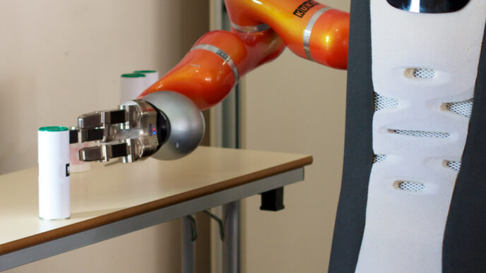 Orange robot arm with a silver three-fingered gripper on a Care-O-bot service robot, reaching for a small white canister with a green cap on a table