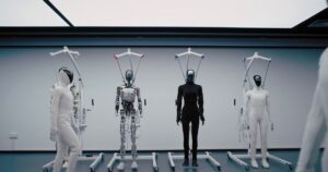 Four XPENG IRON humanoid robots hang from white support stands in a bright studio: one in a white covering, one with its metal frame and wiring exposed, one in black and one in white